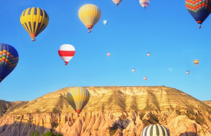 Hot-air balloons in blue sky above mountain range.